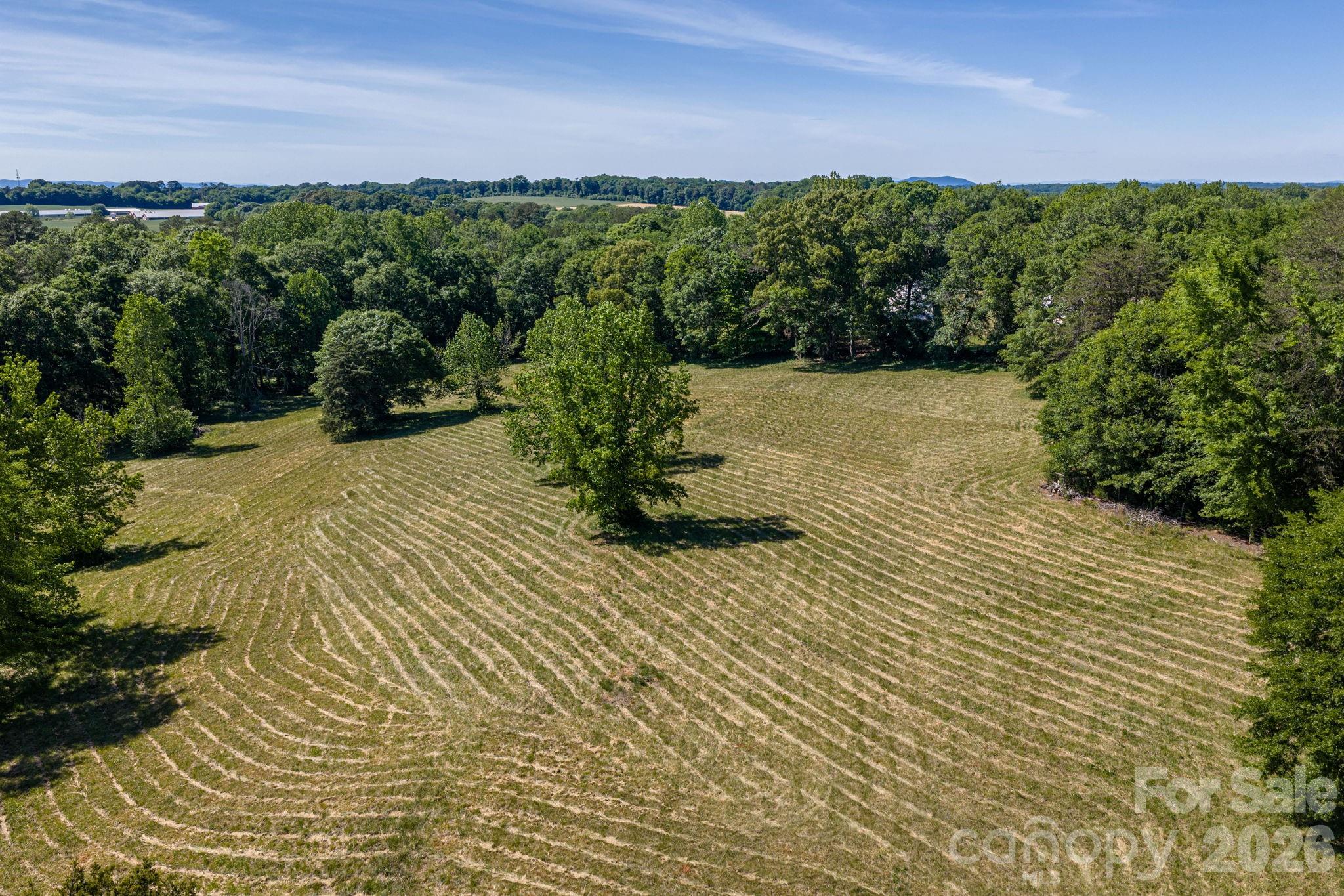 Aerial view of a mowed field bordered by trees, with scattered trees and distant wooded hills.