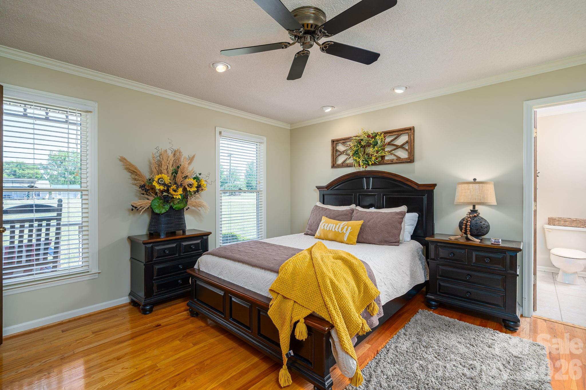 Bedroom with a dark wood bed, yellow throw, hardwood floors, and an adjoining bathroom.