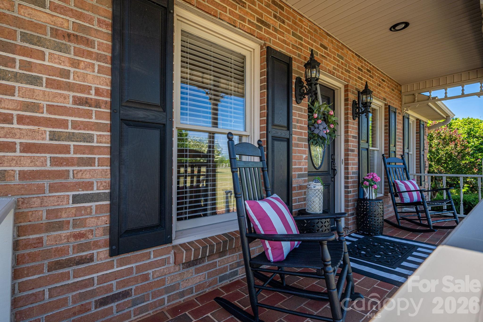 Brick front porch with rocking chairs, striped cushions, and potted flowers.