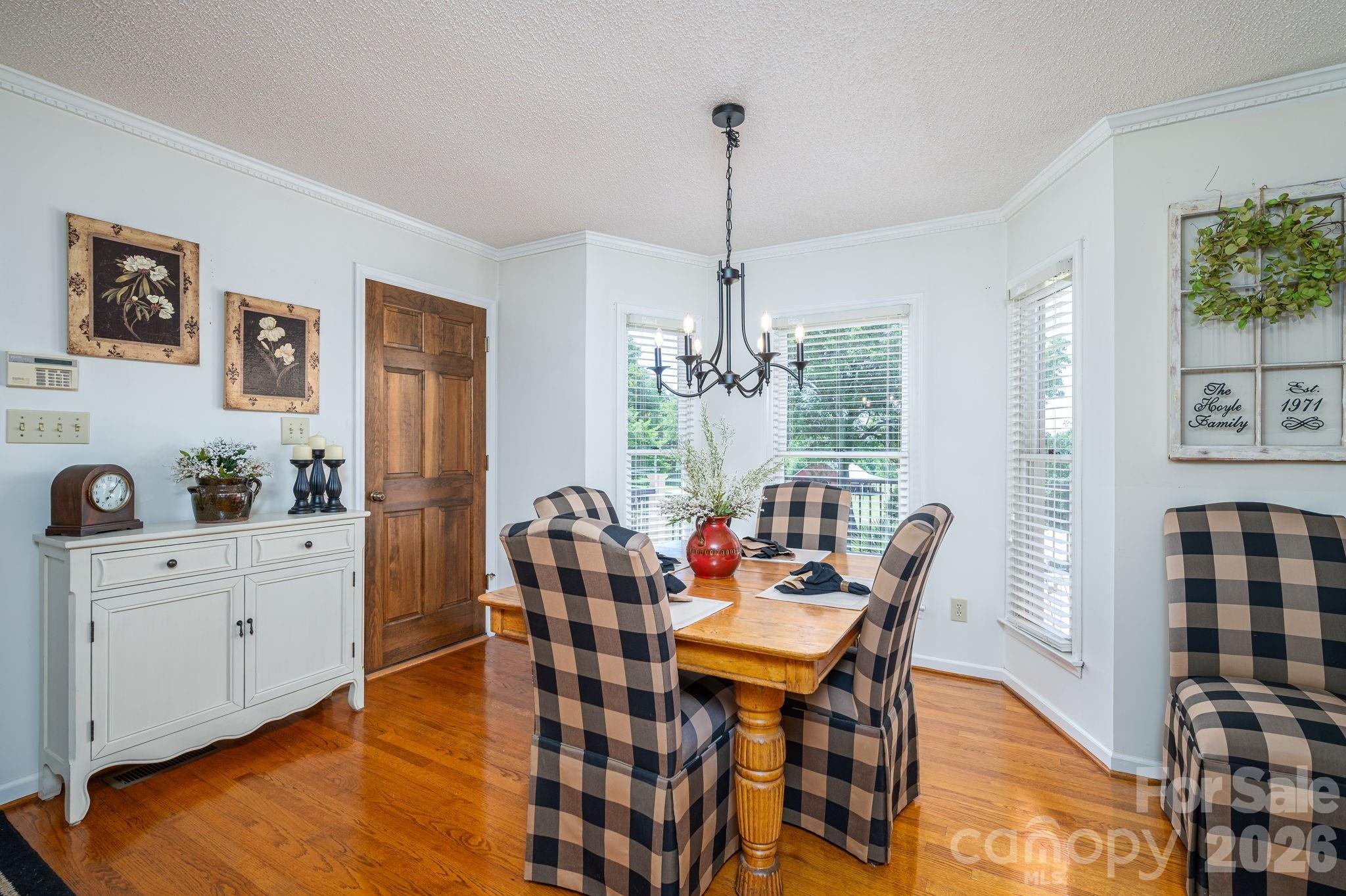 Dining room with a wooden table, checkered chairs, hardwood floors, and a black chandelier.