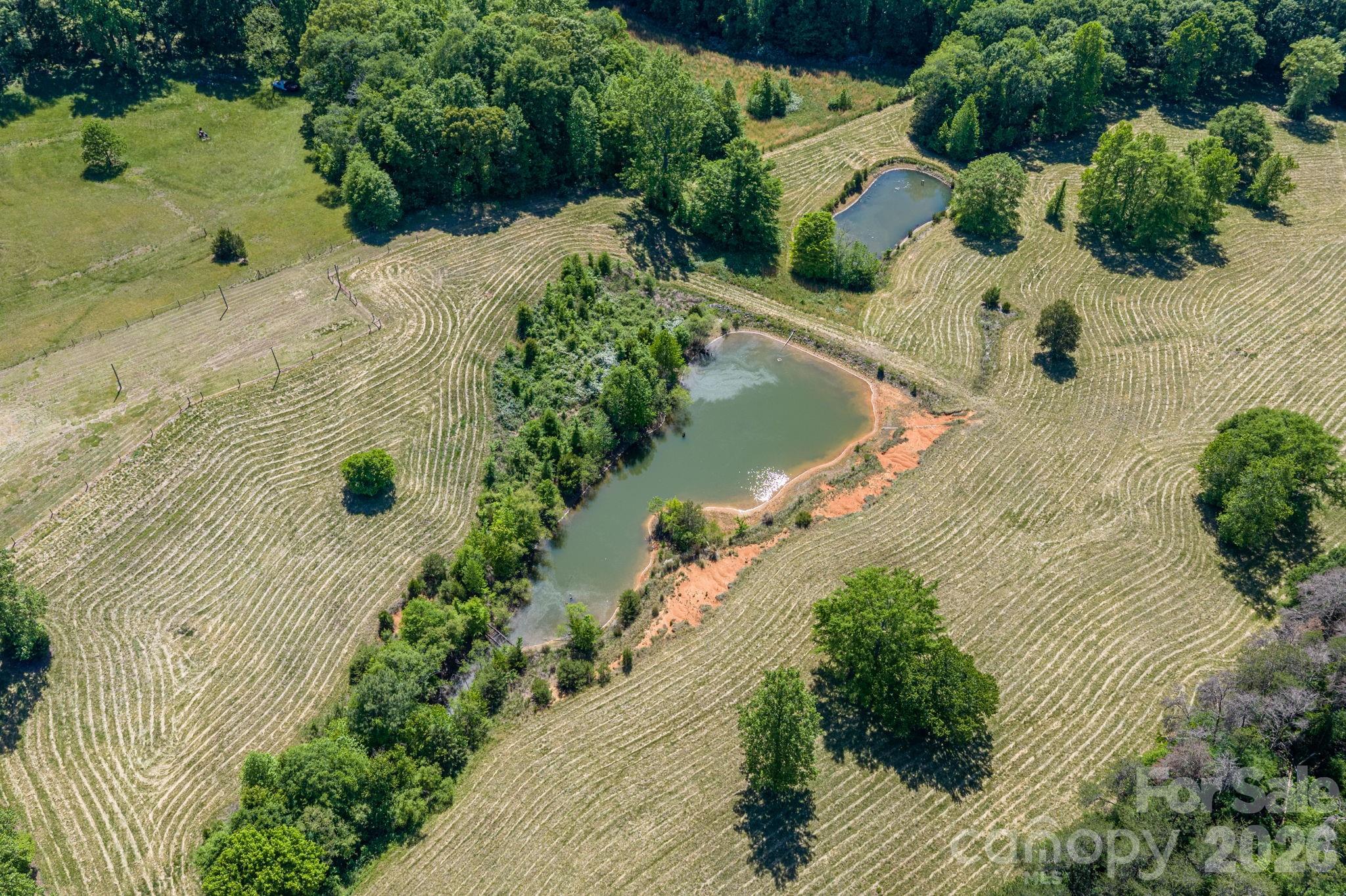 Aerial view of mowed acreage with two ponds, scattered trees, and wooded borders.