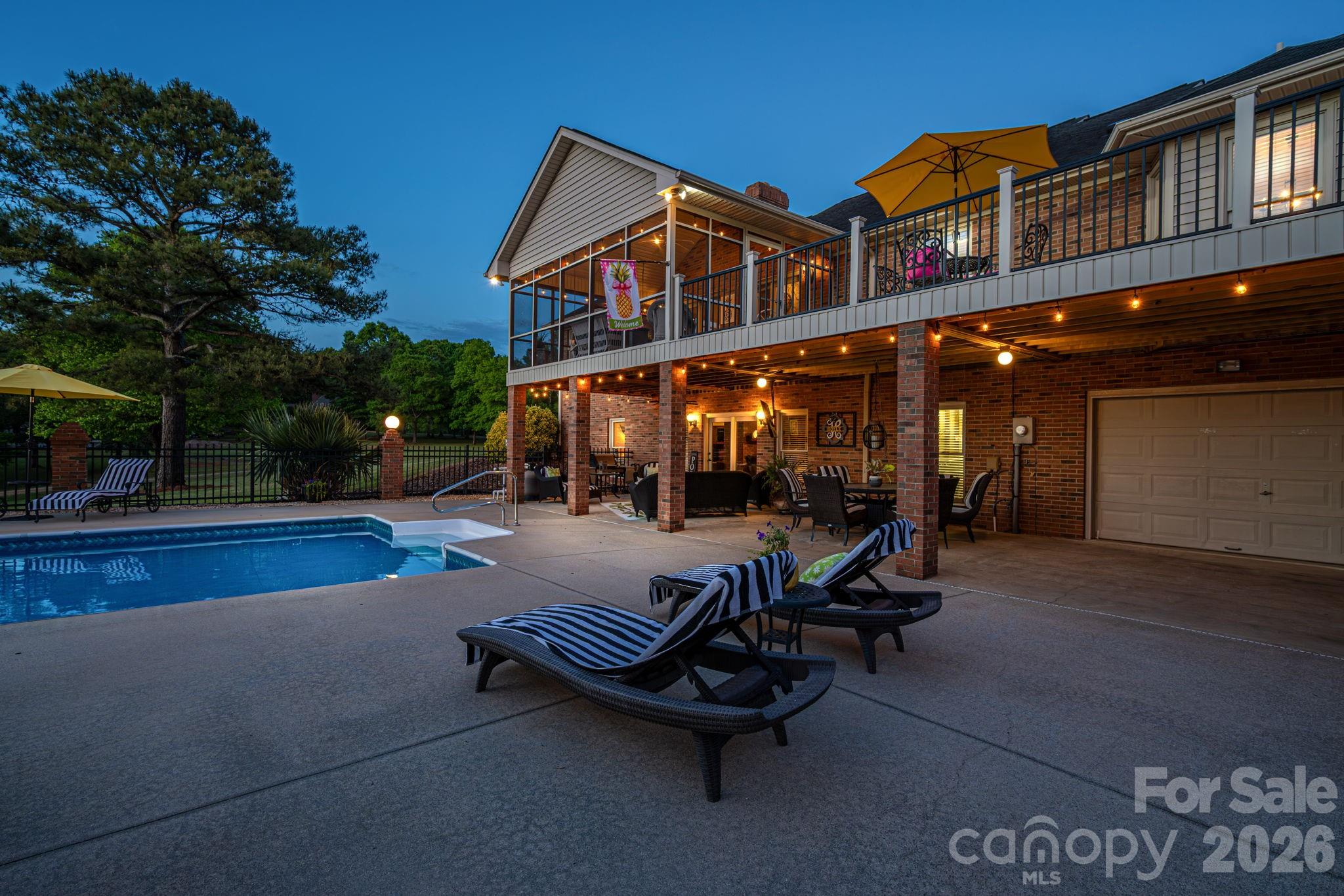 Brick home with a pool and furnished covered patio at dusk.