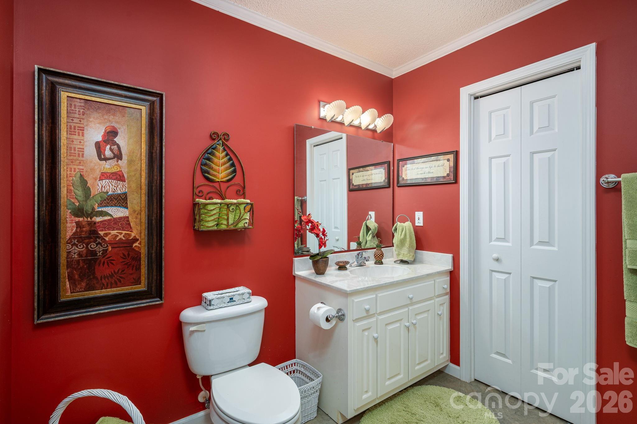 Bathroom with deep red walls, white vanity and toilet, and framed artwork.
