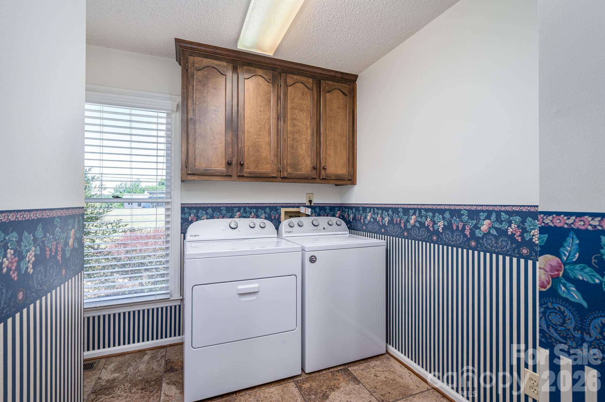 Laundry room with white washer and dryer, dark wood cabinets, and blue floral and striped wallpaper.