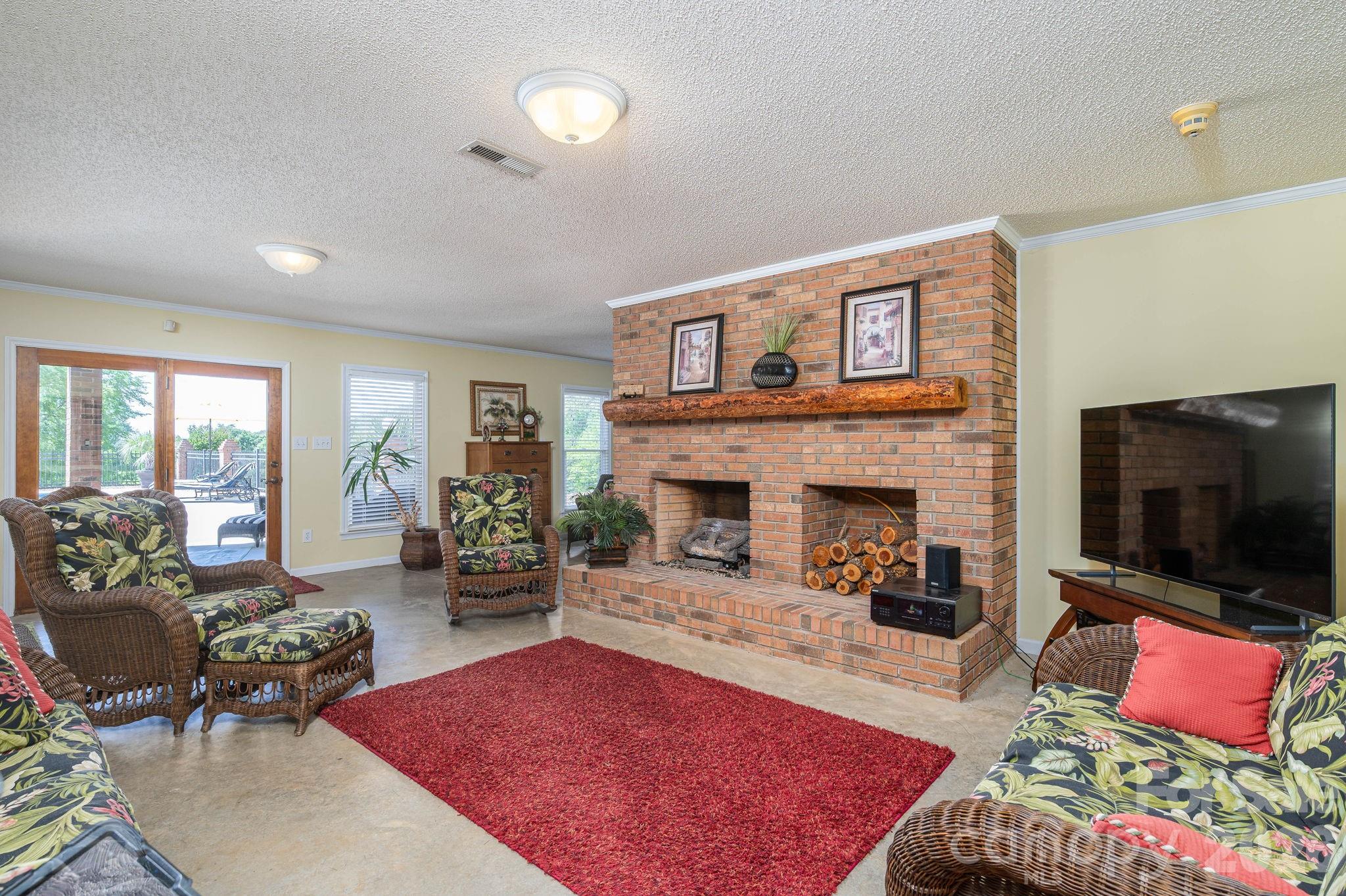 Living room with a large brick fireplace, wicker seating, and a red area rug.