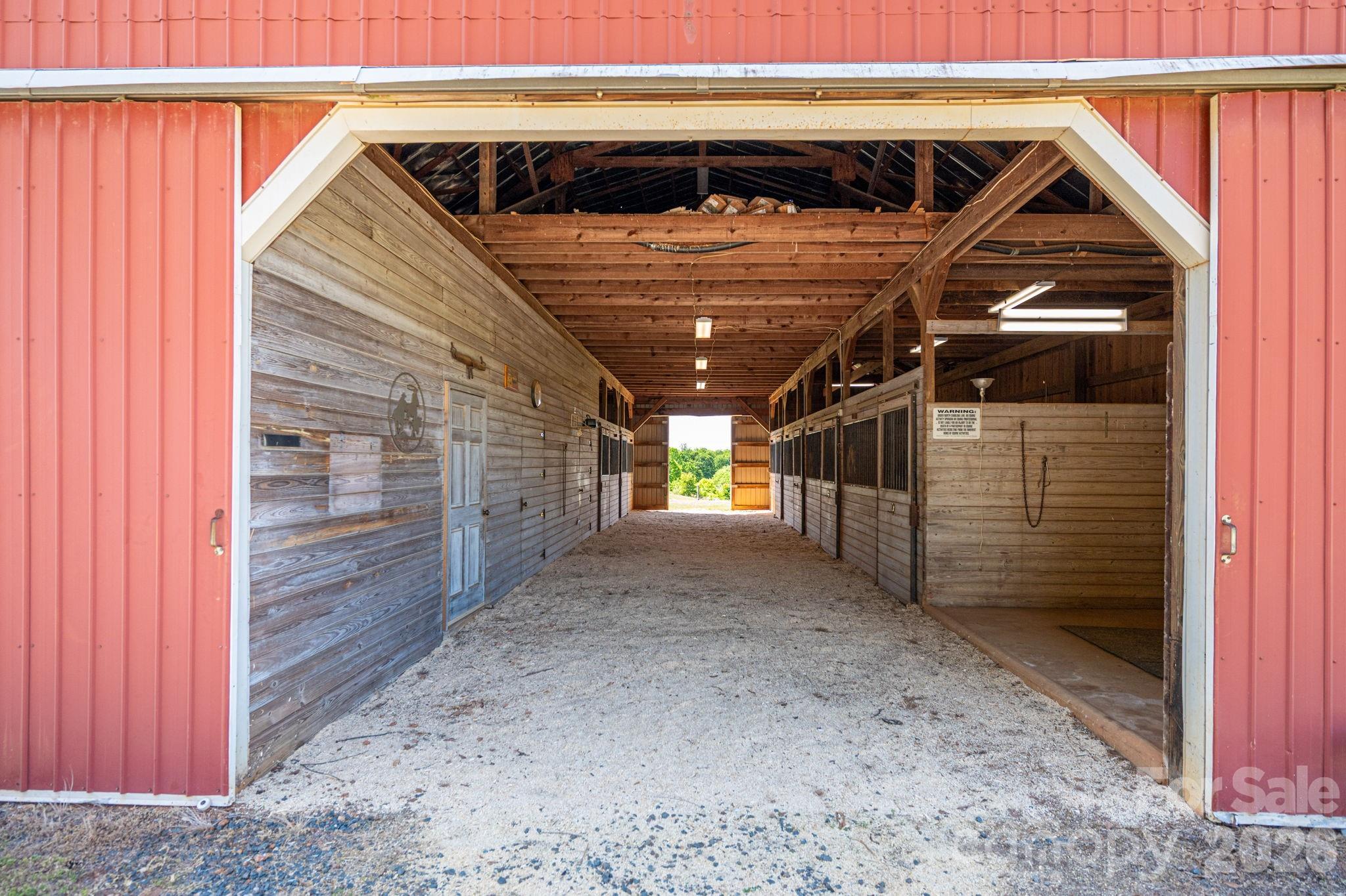 Horse barn interior with a gravel aisle between wooden stalls and exposed timber rafters.