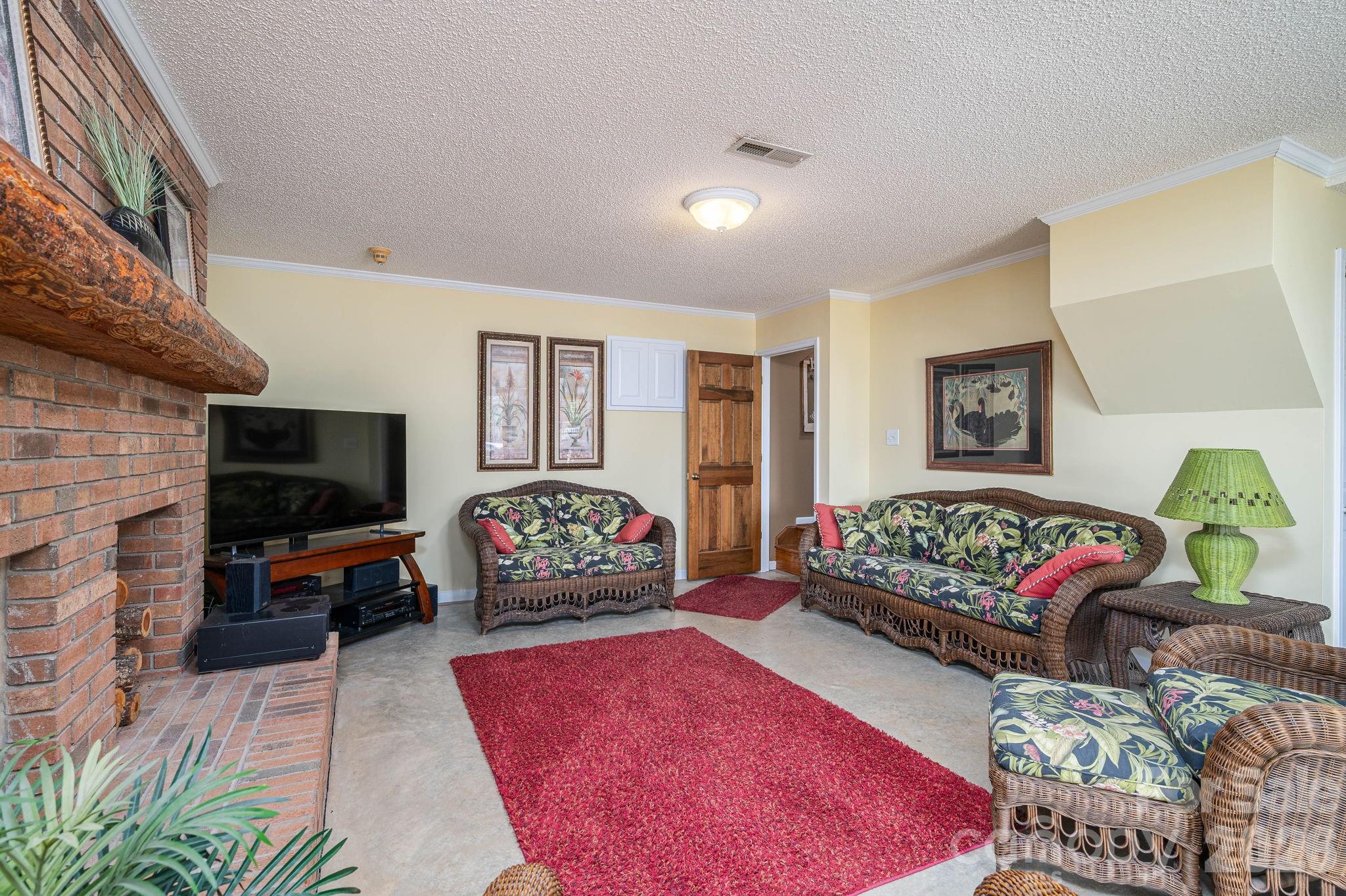 Living room with a brick fireplace, floral wicker seating, and red rugs.