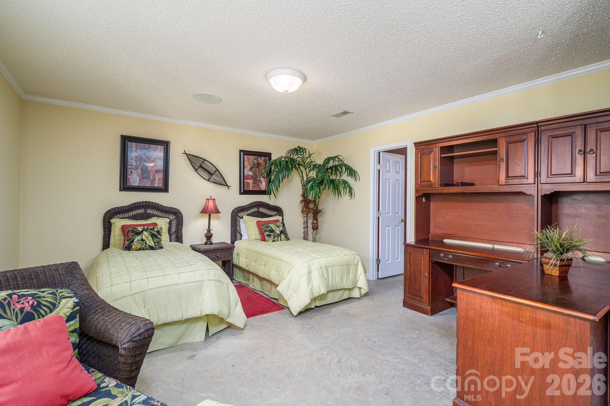 Furnished bedroom with two twin beds, wicker furniture, and built-in wooden cabinetry.