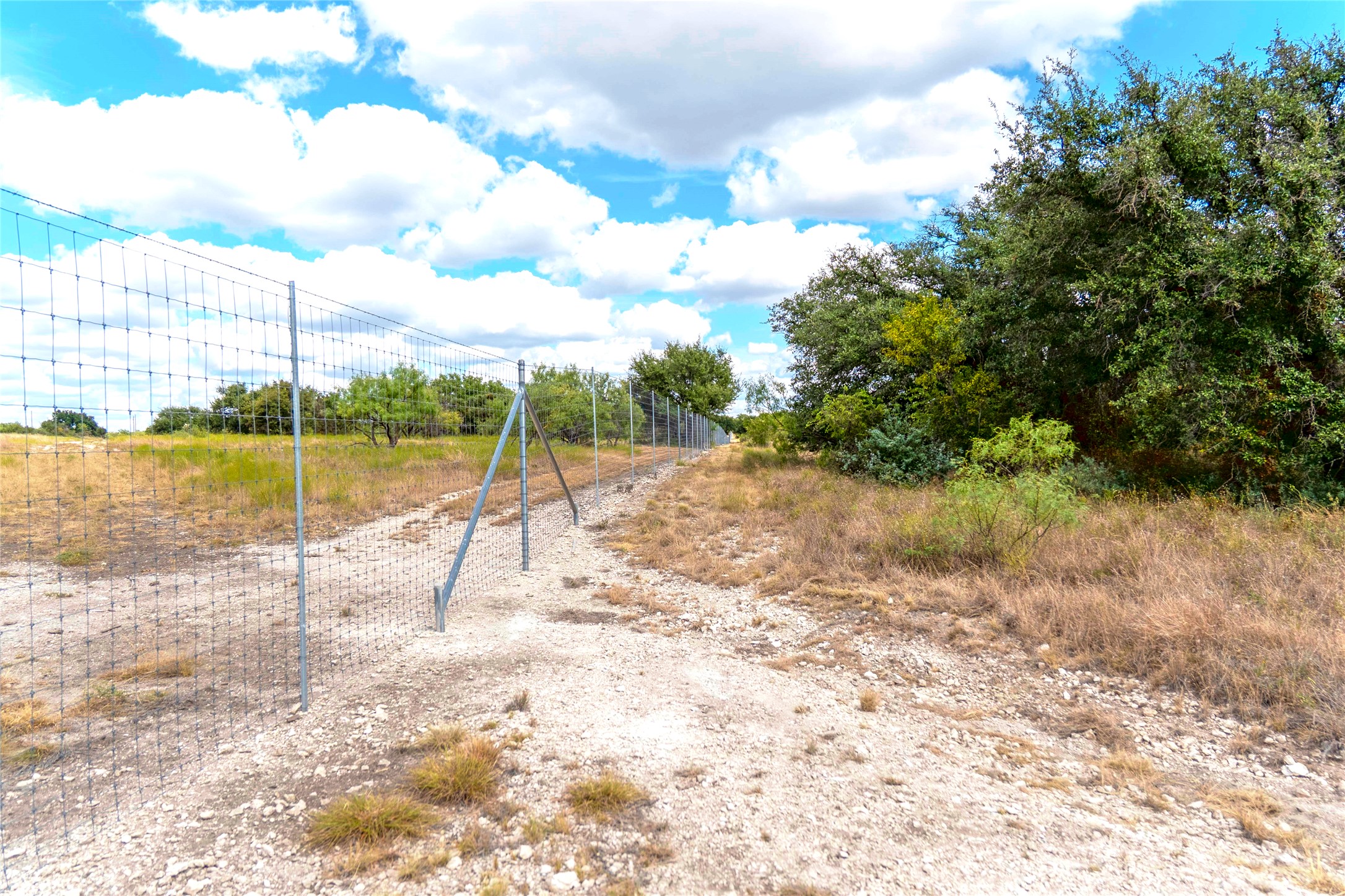 Fenced rural property with a rocky track, dry grass, and mature trees.
