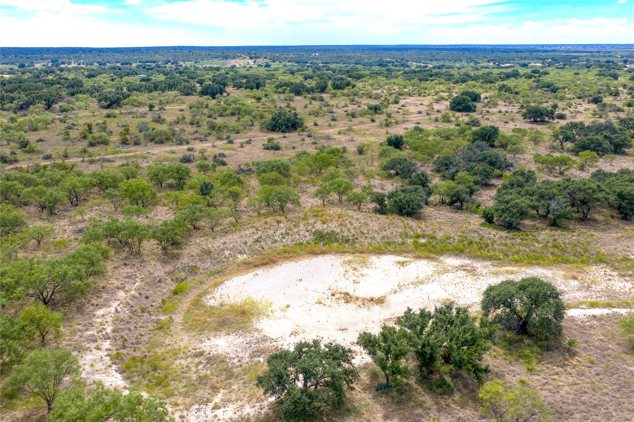 Aerial view of scrub-covered acreage with a broad pale clearing and scattered trees.