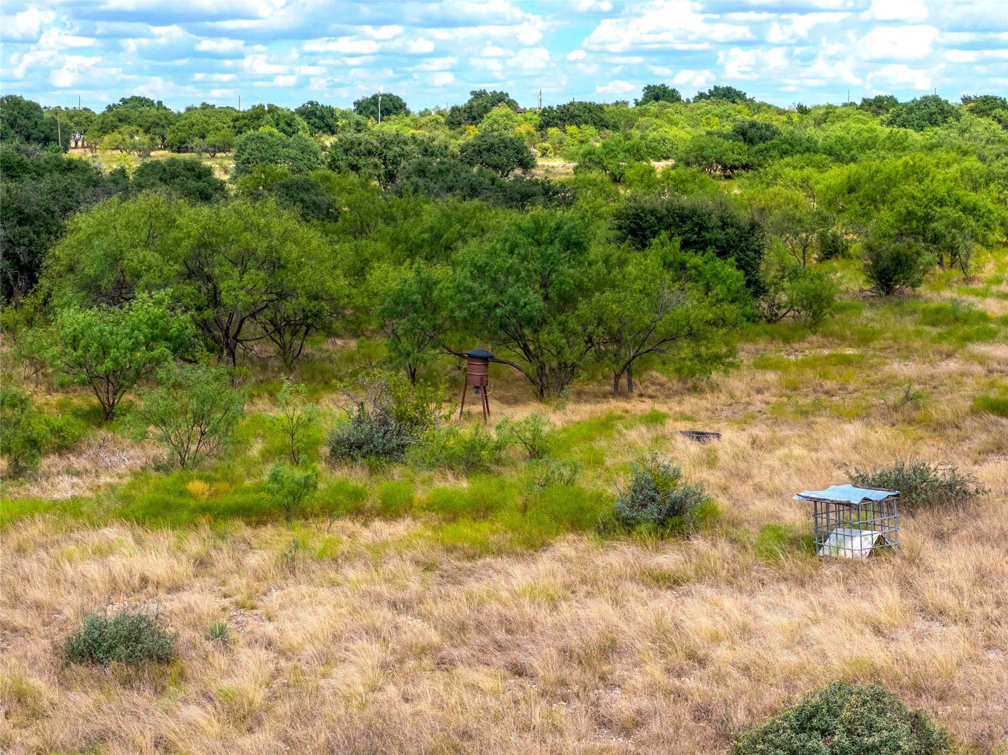 Rural acreage with scattered trees, a deer feeder, and a covered water trough.