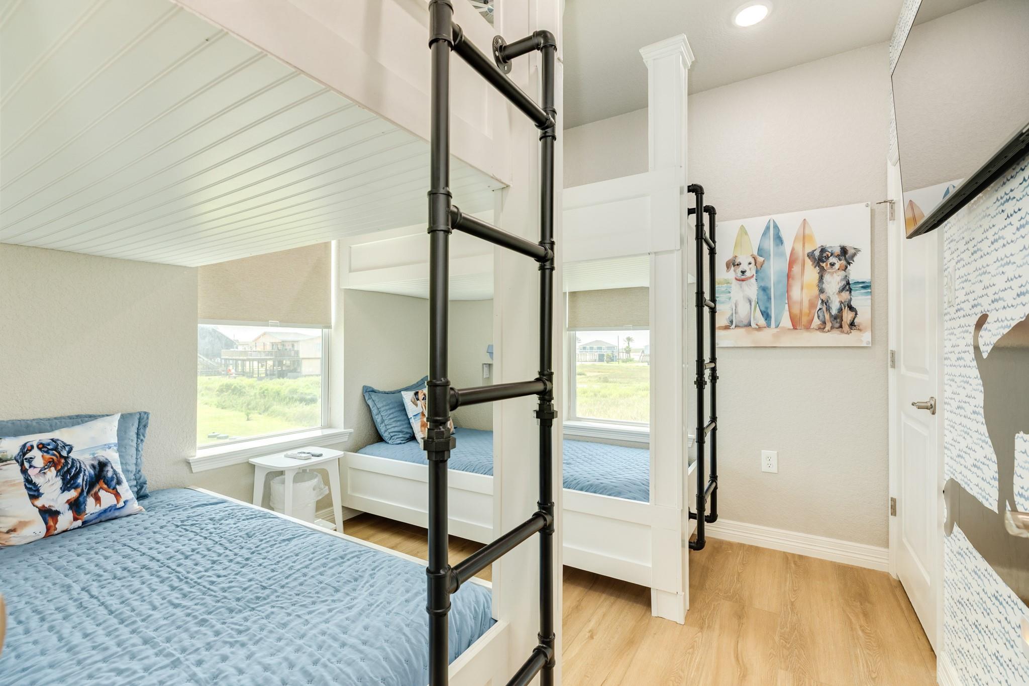 Bright bedroom with built-in twin bunks, blue bedding, large windows, and coastal dog artwork.