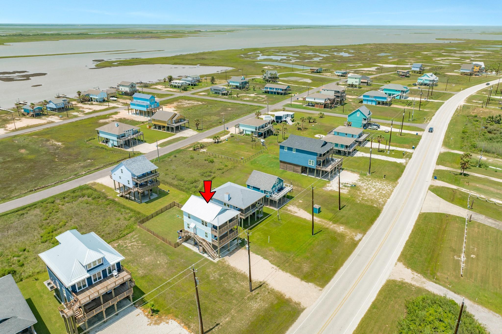 Elevated coastal home marked by a red arrow, surrounded by marshland and neighboring houses.