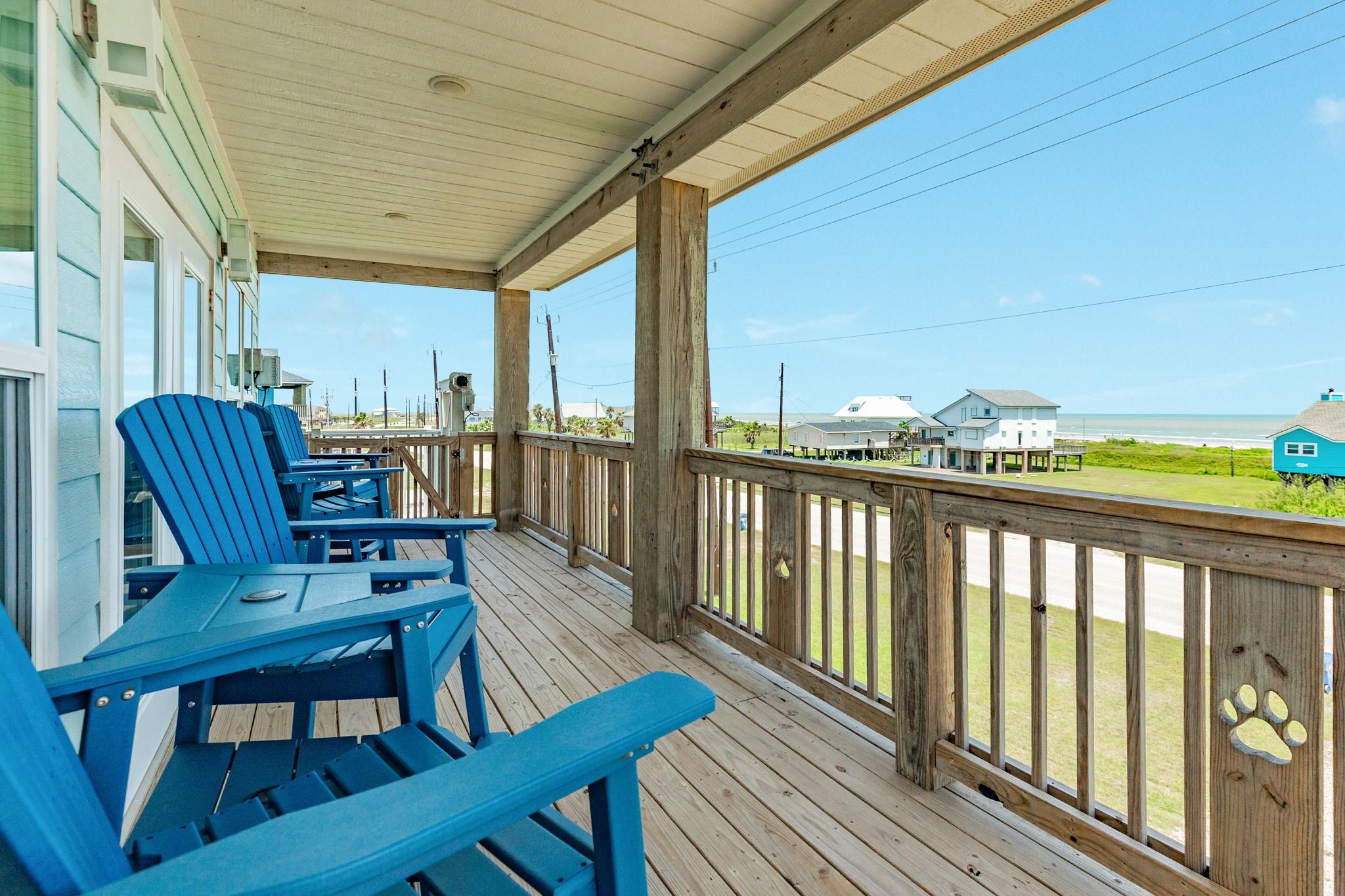 Covered wooden deck with blue Adirondack chairs overlooking the Gulf shoreline.
