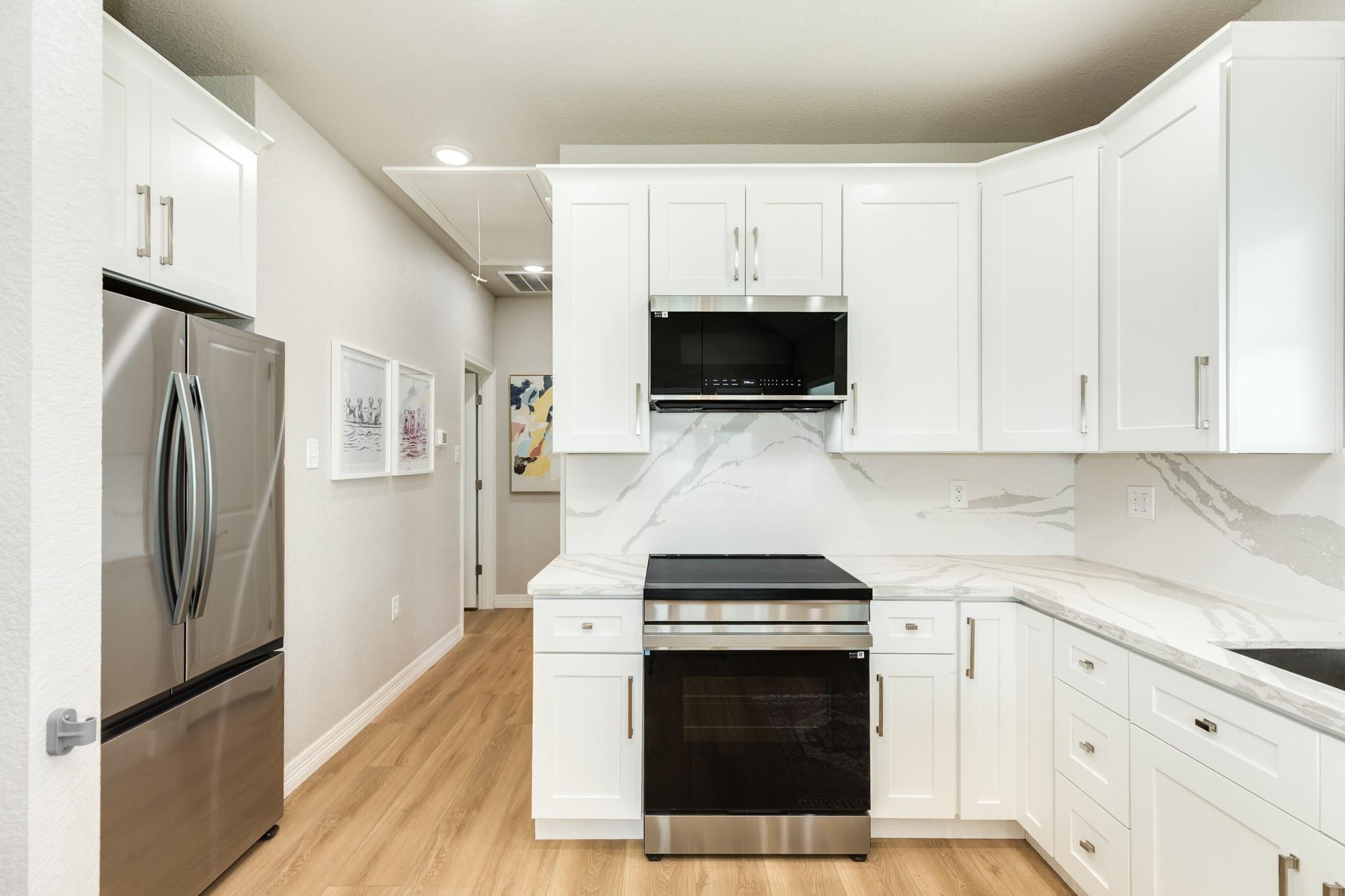 Kitchen with white cabinets, veined countertops, and stainless steel appliances.