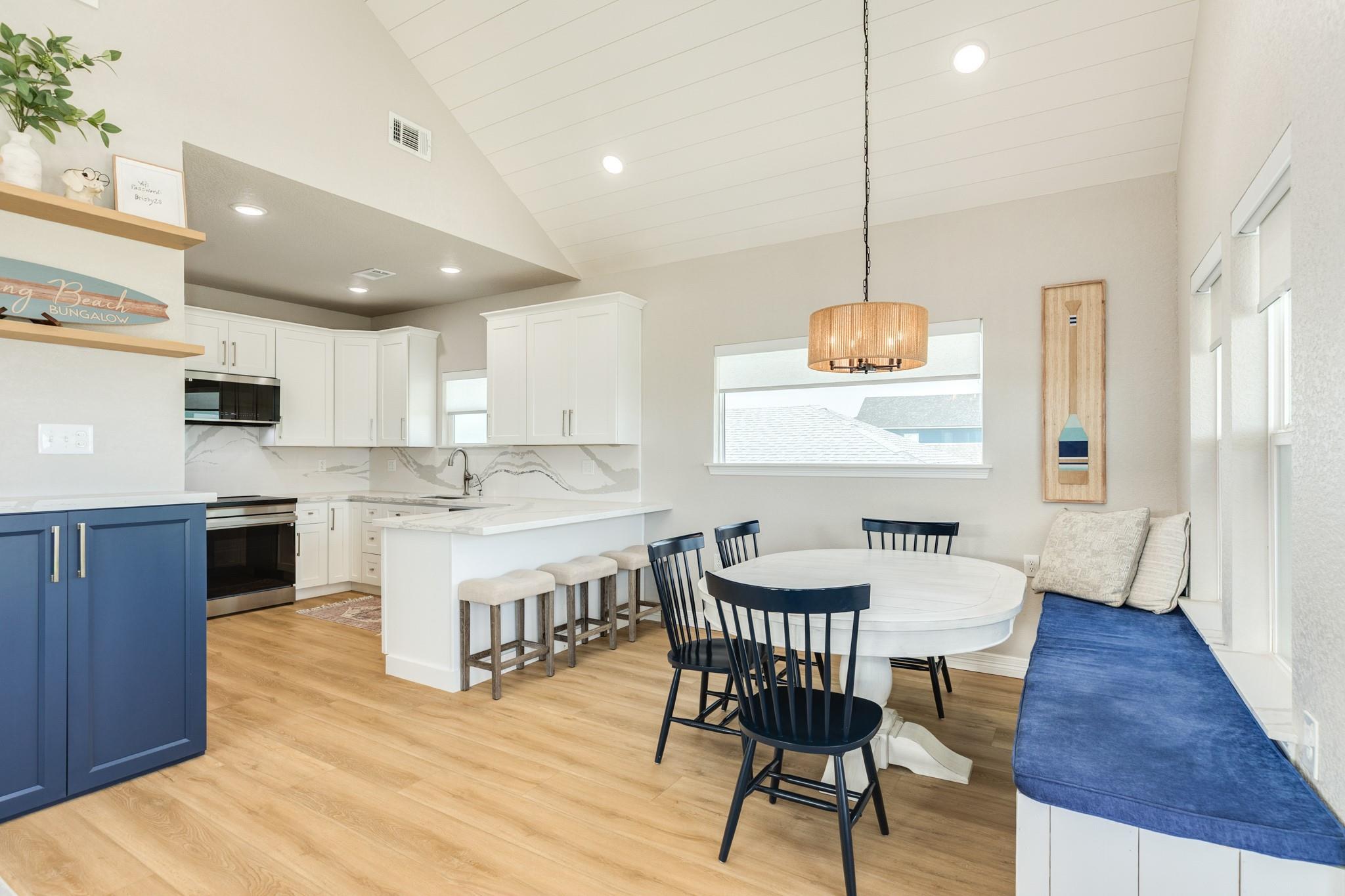 Kitchen and dining area with a blue island, round table, and window bench.
