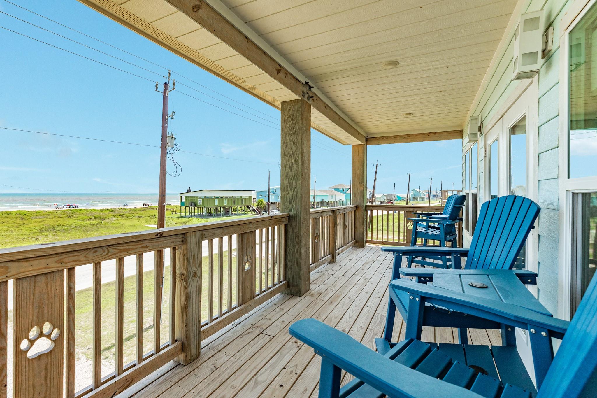 Covered beachfront porch with blue Adirondack chairs overlooking grassy dunes and the ocean.