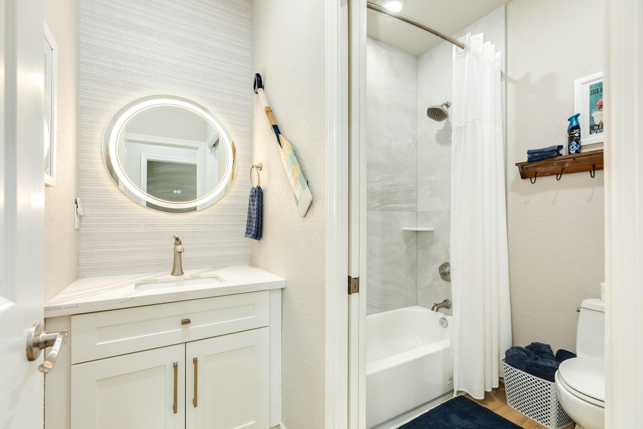Bathroom with an illuminated round mirror, white vanity, tub and shower, and navy accents.