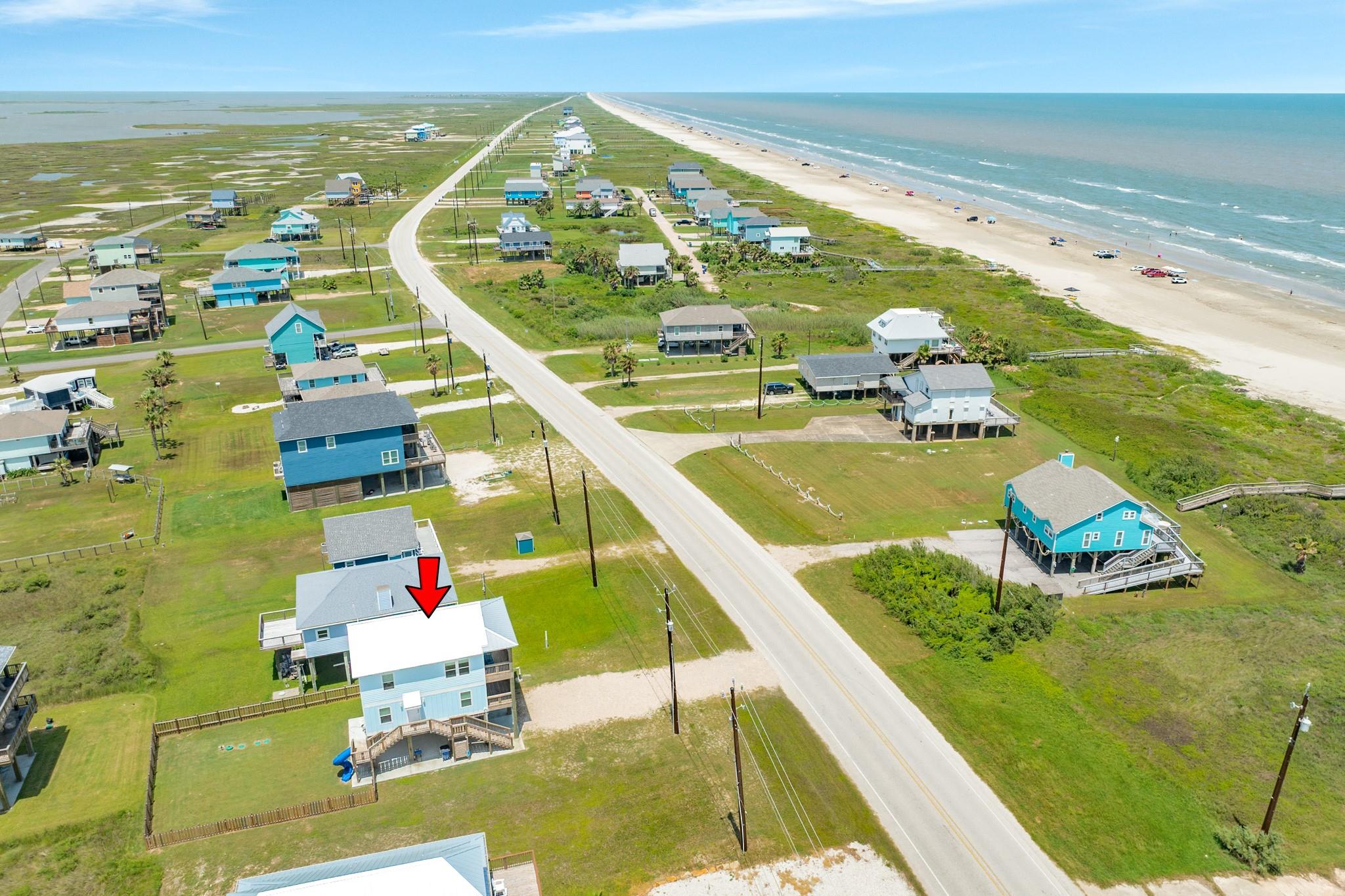 Pale blue raised coastal house marked by a red arrow, near the beach and Blue Water Highway.