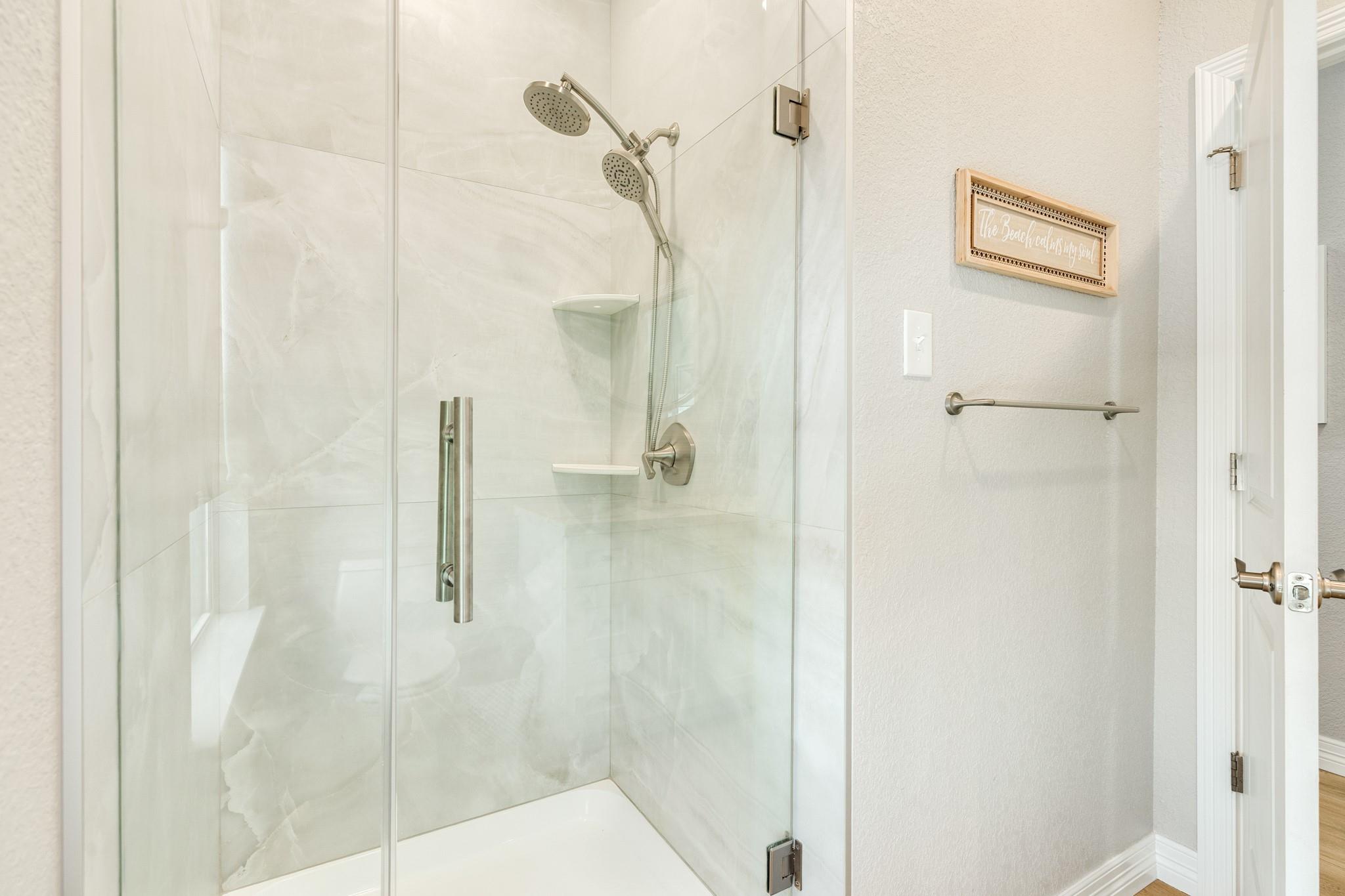 Glass-enclosed bathroom shower with pale tile, dual showerheads, and brushed metal fixtures.