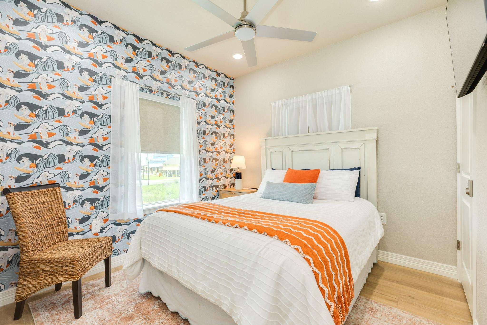 Bedroom with cat-and-wave wallpaper, a white bed with orange accents, and a woven chair.