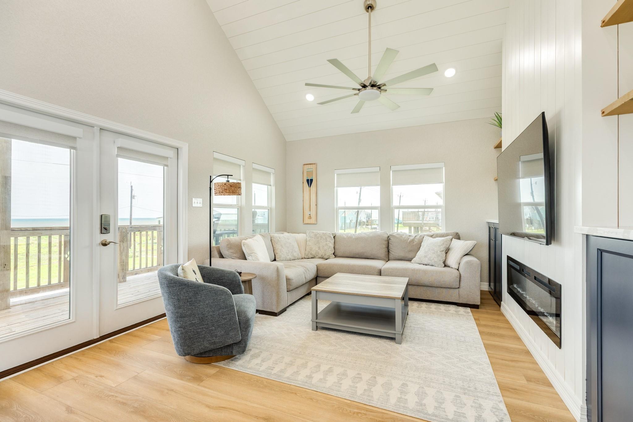 Furnished living room with vaulted ceiling, sectional sofa, fireplace, and a deck with water views.