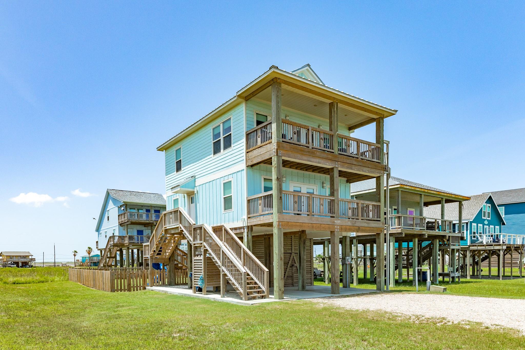 Pale aqua elevated coastal house with two covered wooden decks and exterior stairs.