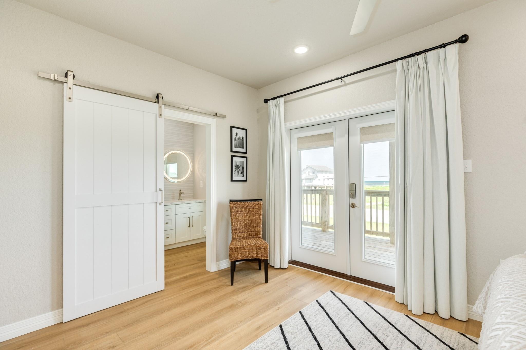 Bedroom with a barn door to the bathroom and deck doors overlooking the ocean.