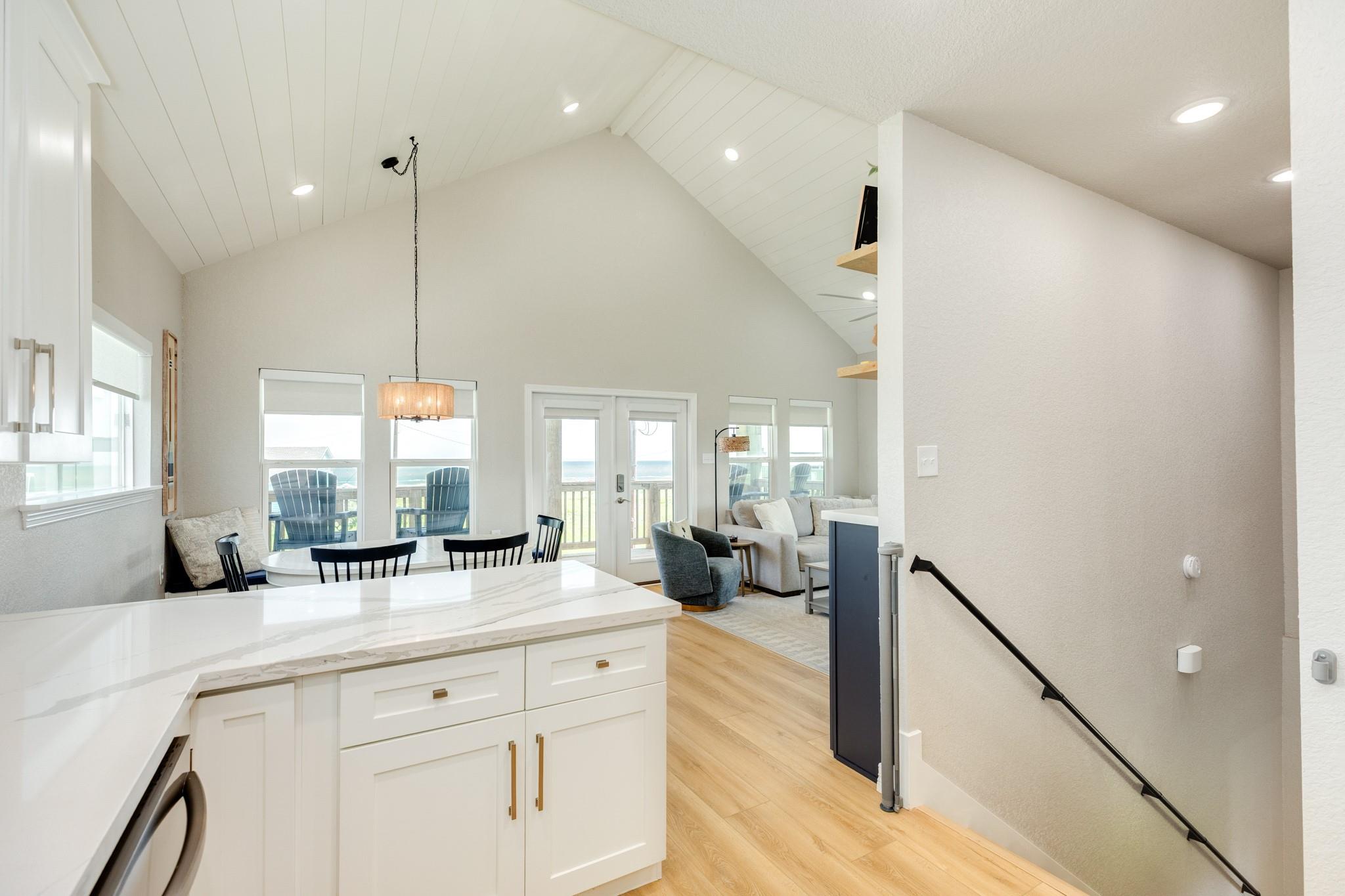 Open-plan kitchen and living area with vaulted ceiling, white island, and ocean views through the windows.