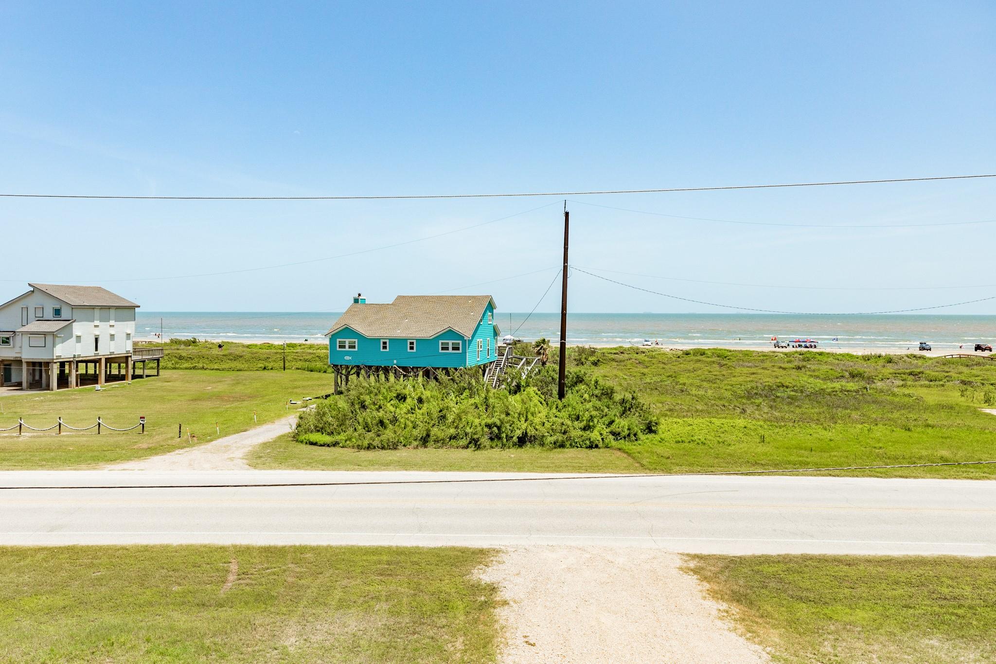 Turquoise elevated beach house with the ocean and grassy dunes behind it