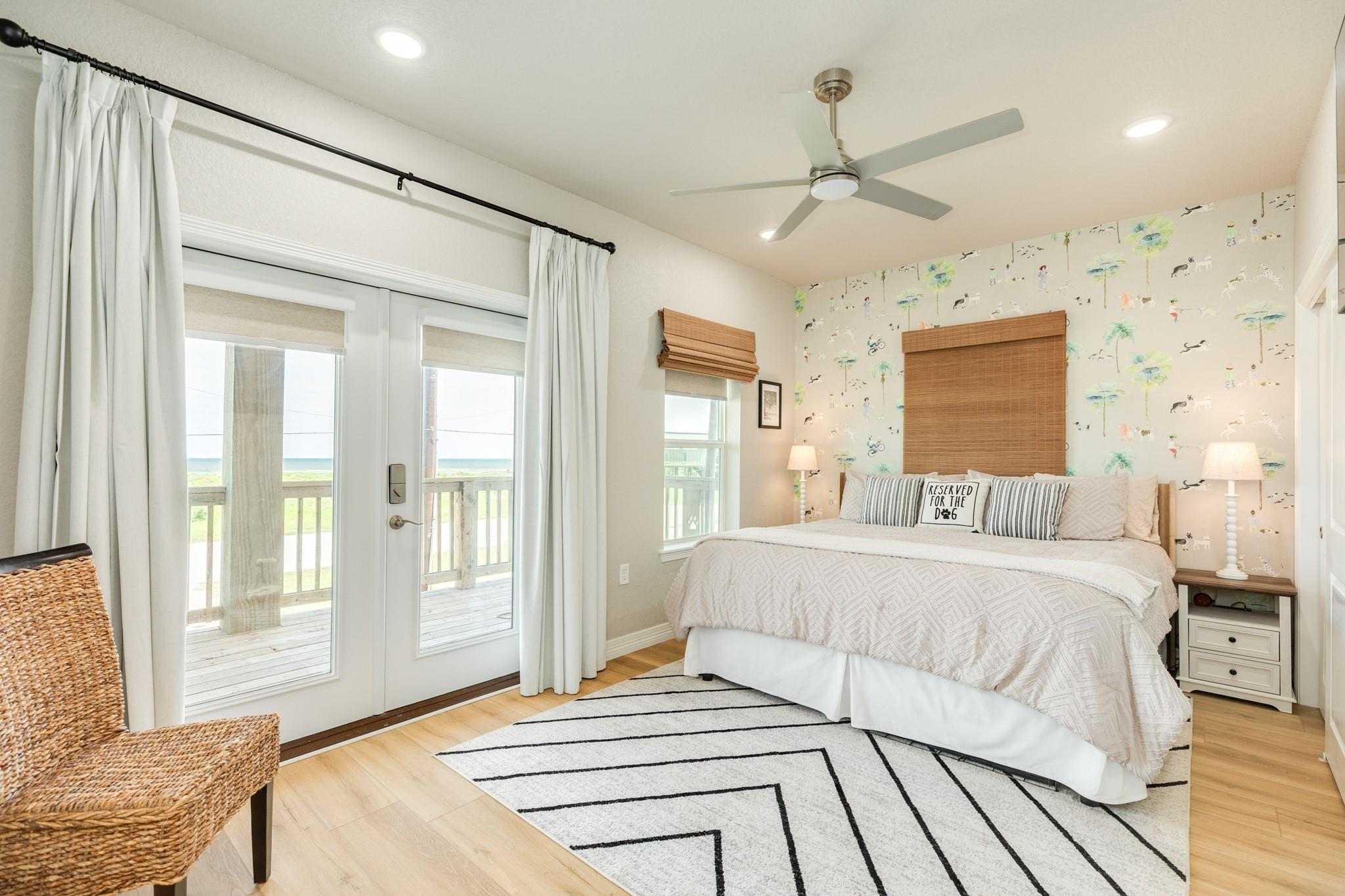 Bedroom with a white bed, patterned accent wall, and glass doors overlooking water.