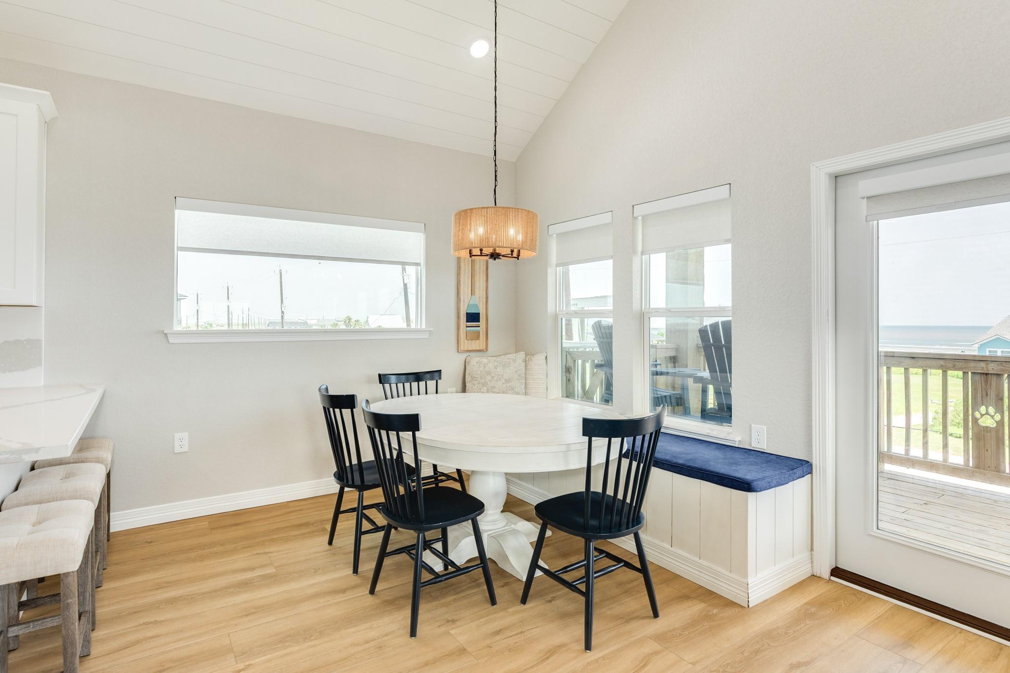 Dining area with a white oval table, black chairs, and ocean views through the windows.