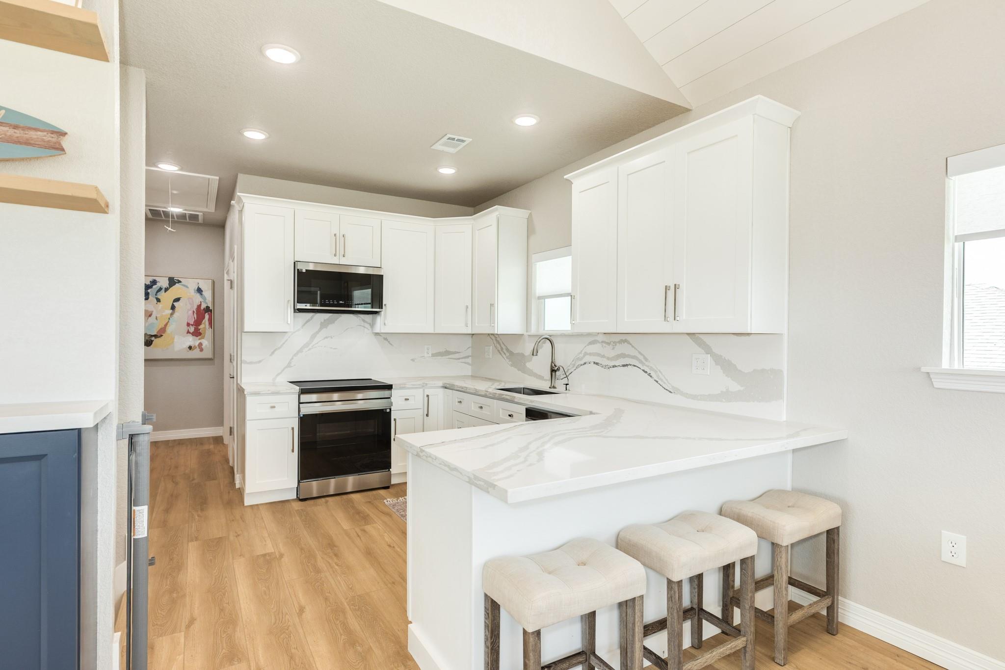 Kitchen with white cabinets, veined stone counters, stainless steel appliances, and a peninsula with three stools.