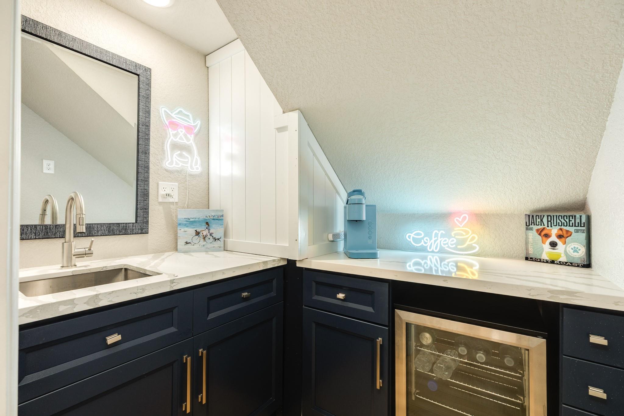 Under-stair coffee bar with navy cabinets, a sink, coffee machine, and glass-front wine refrigerator.