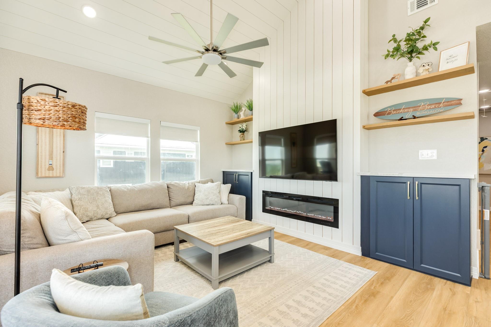 Furnished living room with beige sectional, television, linear fireplace, and navy-blue cabinets.