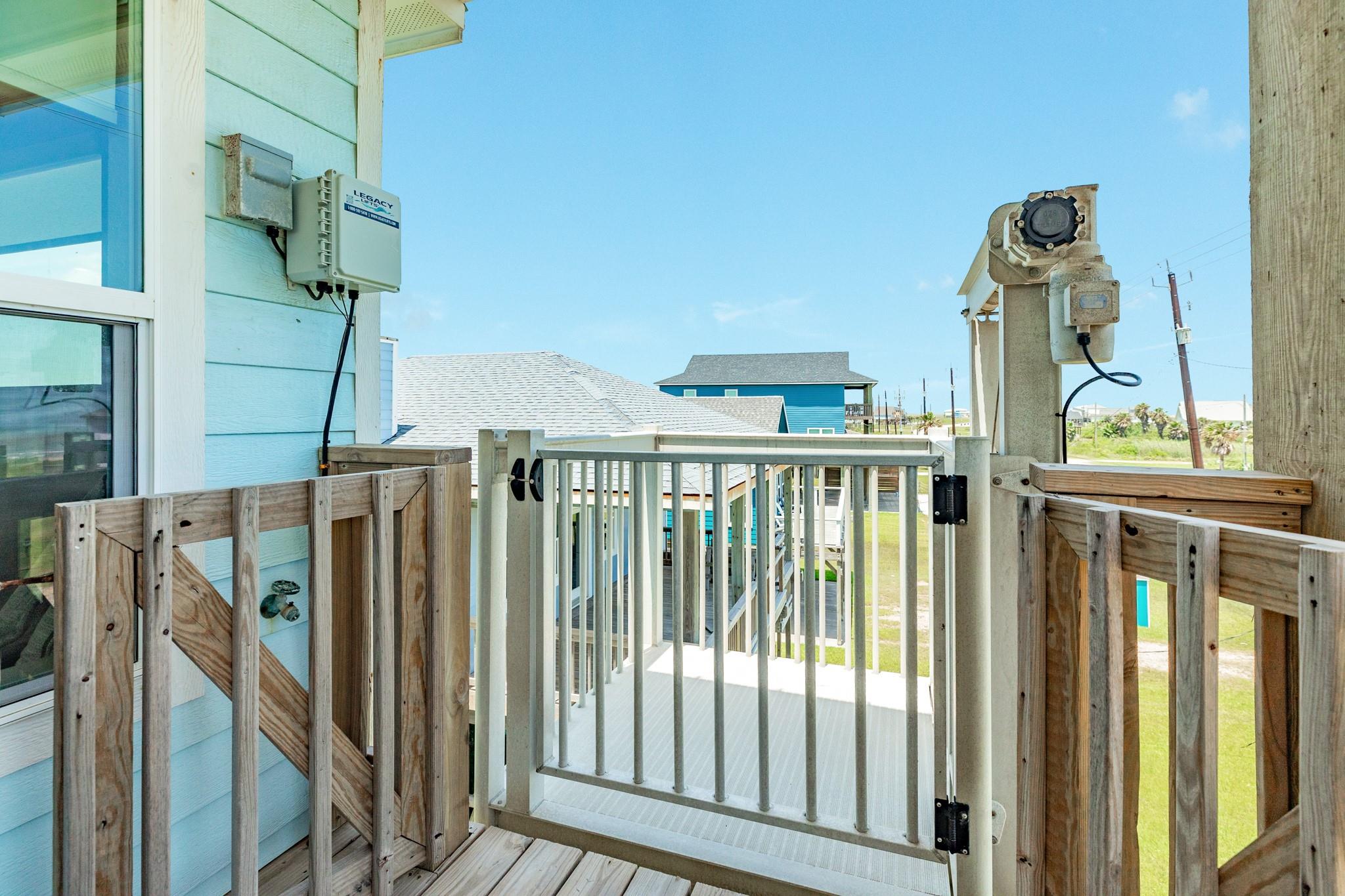 Elevated deck with white railing and lift equipment overlooking nearby homes and a grassy yard.