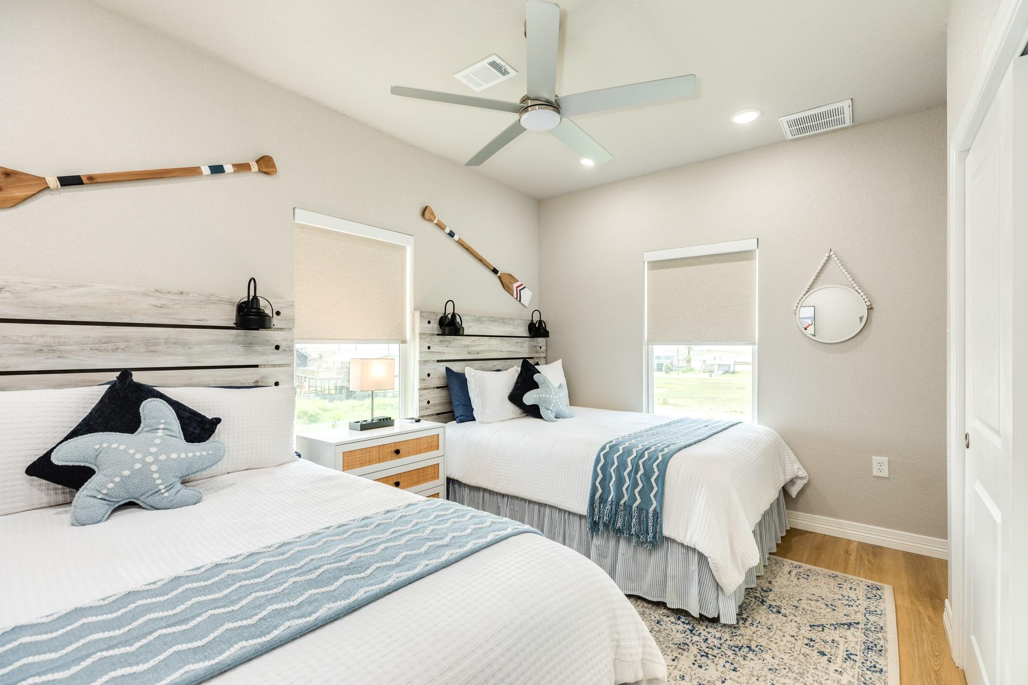 Bedroom with two white beds, blue throws, starfish pillows, and coastal paddle decor.