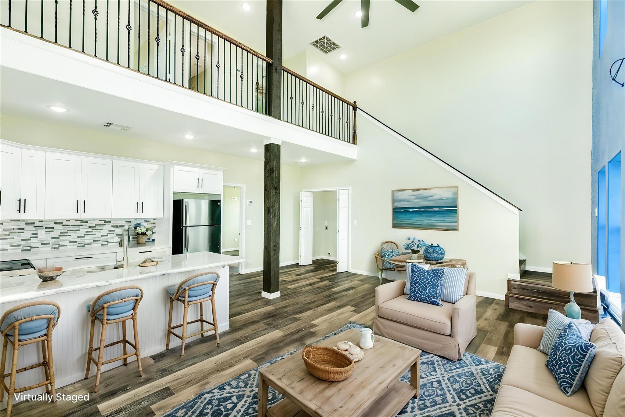 Open-plan living room and kitchen with a mezzanine, white cabinetry, and blue coastal accents.