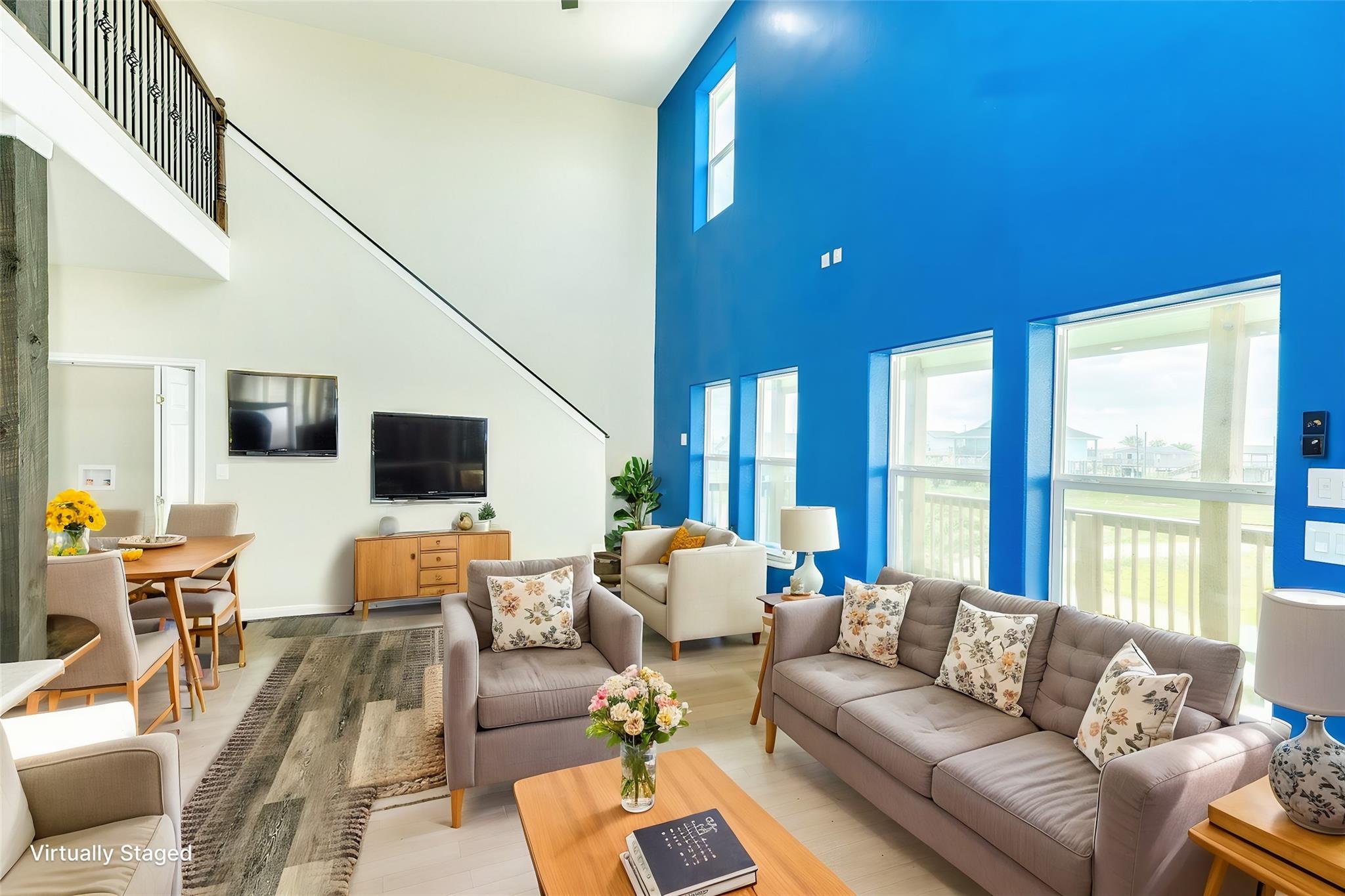 Staged double-height living room with a vivid blue wall, large windows, and staircase.
