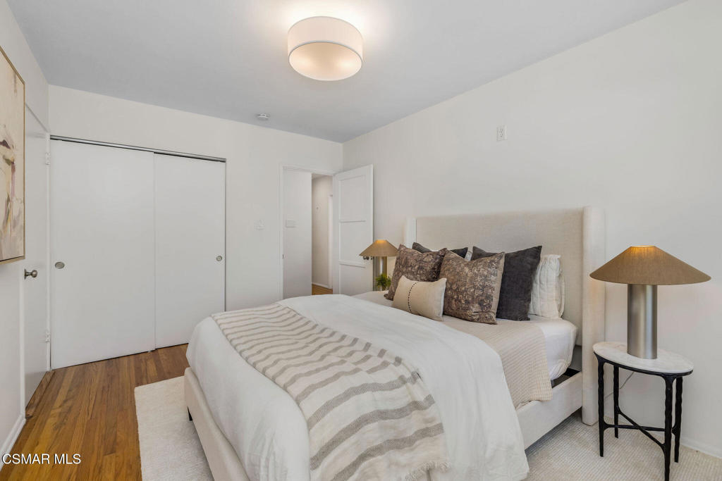 Bedroom with a large white bed, upholstered headboard, patterned pillows, and hardwood flooring.