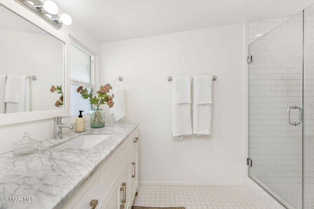 Bathroom with a marble-patterned vanity and glass-enclosed white subway-tile shower.