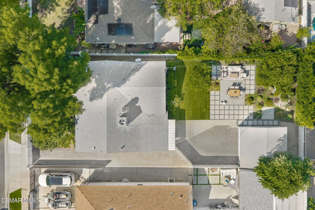 Aerial view of the home and backyard patio, with lawn, trees, driveway, and outdoor dining furniture.