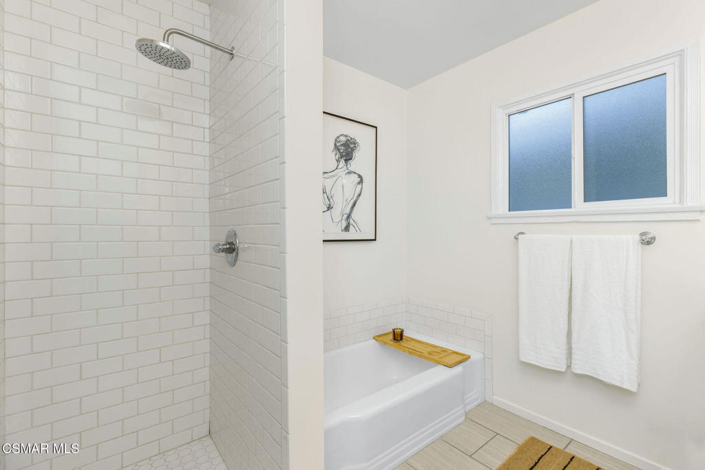 Bathroom with a tiled shower and bathtub beneath a frosted window.