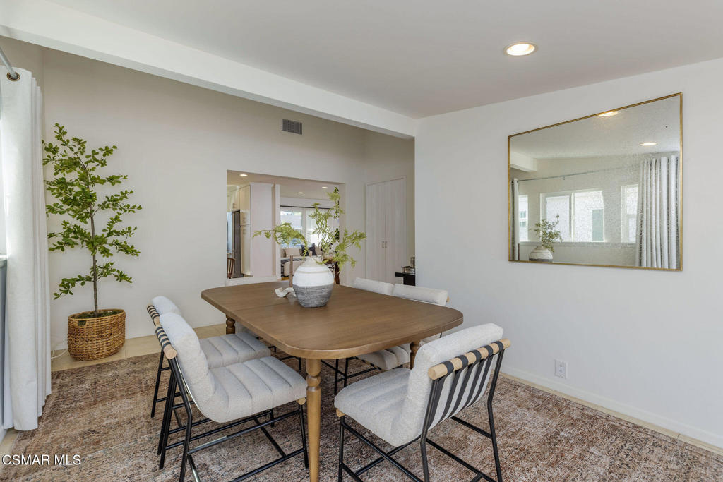 Dining room with a wooden table, upholstered chairs, potted tree, and large wall mirror.
