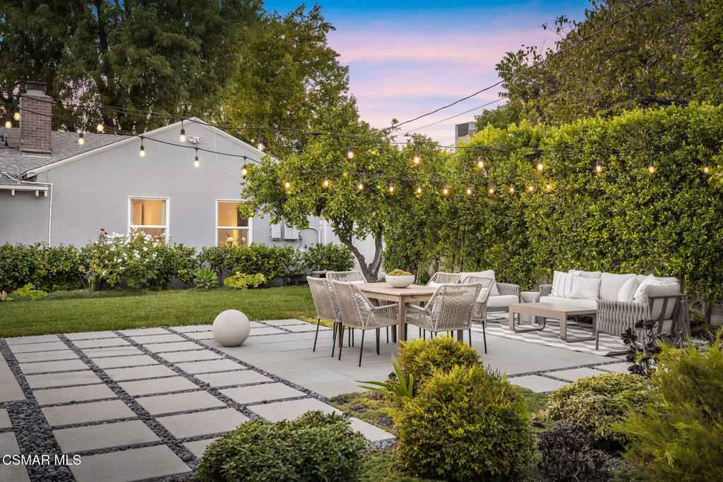 Backyard patio with paved dining area, cushioned lounge seating, and glowing string lights.