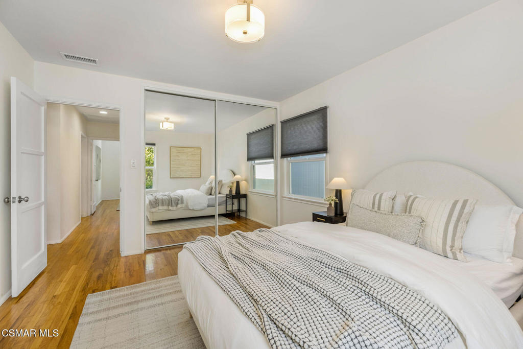 Staged bedroom with a large white bed, mirrored closet doors, and hardwood floors.