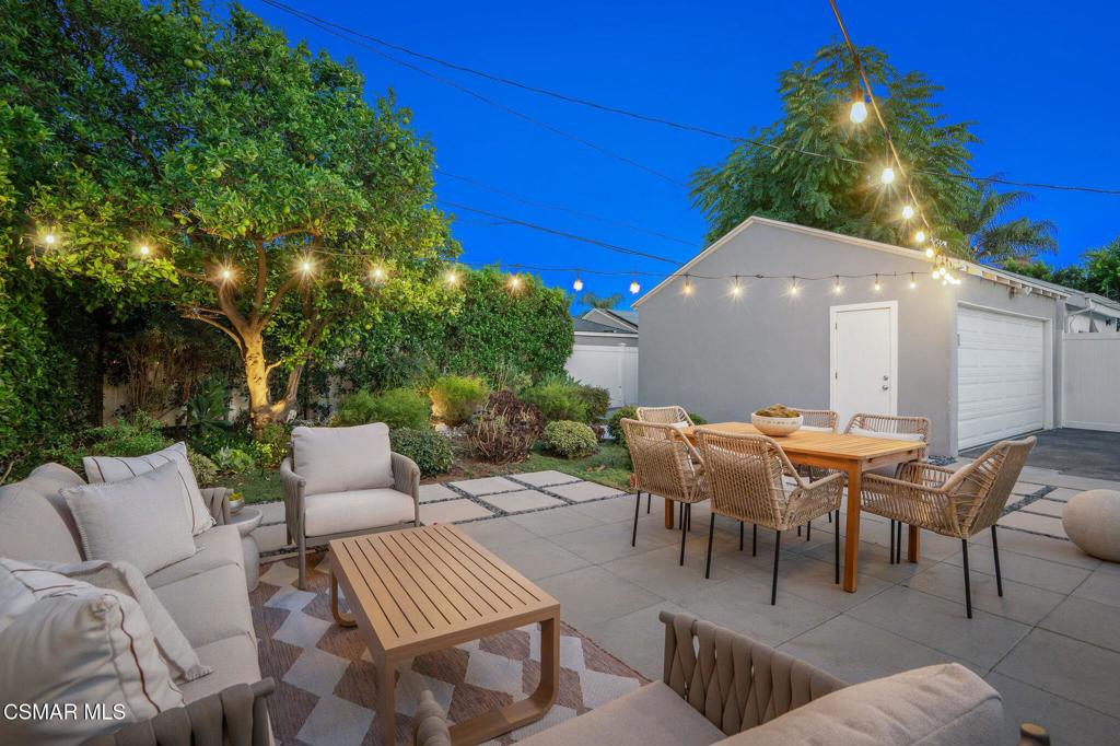 Furnished backyard patio with dining set, lounge seating, and string lights at dusk.