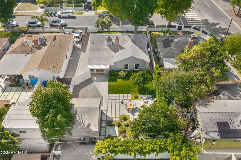 Aerial view of a single-story home with a green lawn and paved backyard patio.
