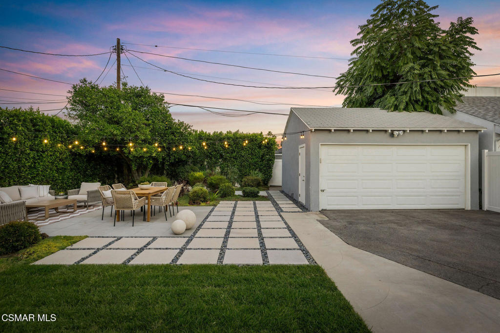 Home exterior with a paved courtyard, outdoor dining area, string lights, and garage at dusk.
