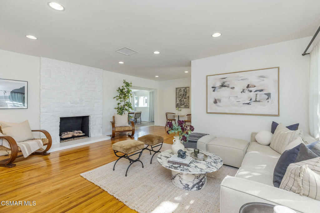 Staged living room with white sofas, a white brick fireplace, hardwood floors, and a round marble coffee table.